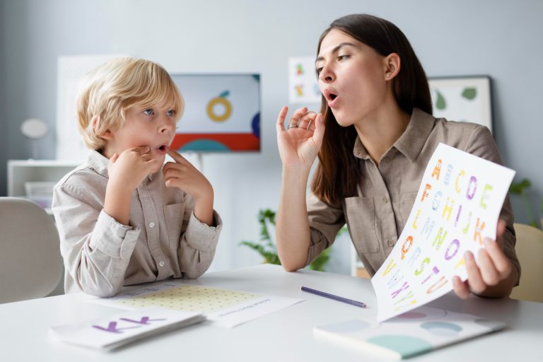 Speech therapist holding an alphabet chart while practicing vocal sounds with a young boy.